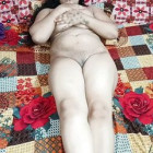 Mollige orientalische Ehefrau mit großen Brüsten liegt mit weit gespreizten Beinen im Bett und fingert ihre blanke Muschi.